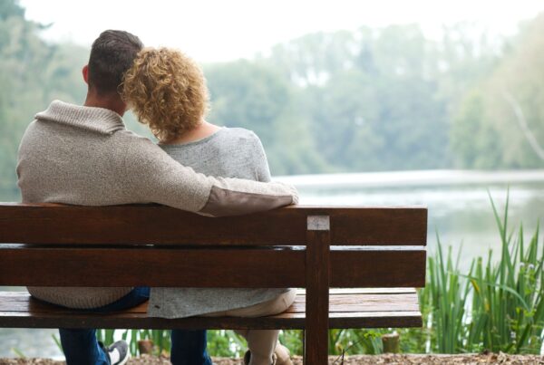 A couple sitting on a park bench, looking out at a lake